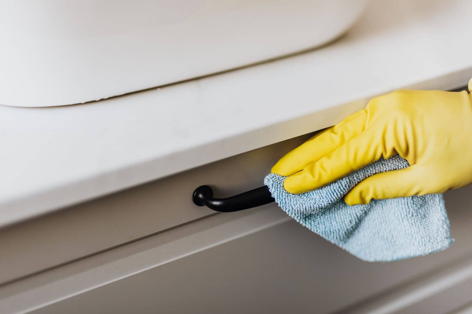 A gloved hand wiping a bright kitchen counter with a microfiber cloth during a deep clean